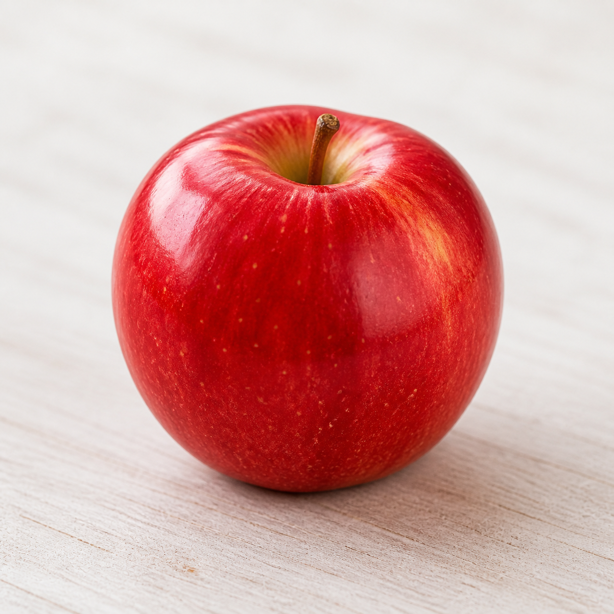 A whole red apple on a light wooden surface