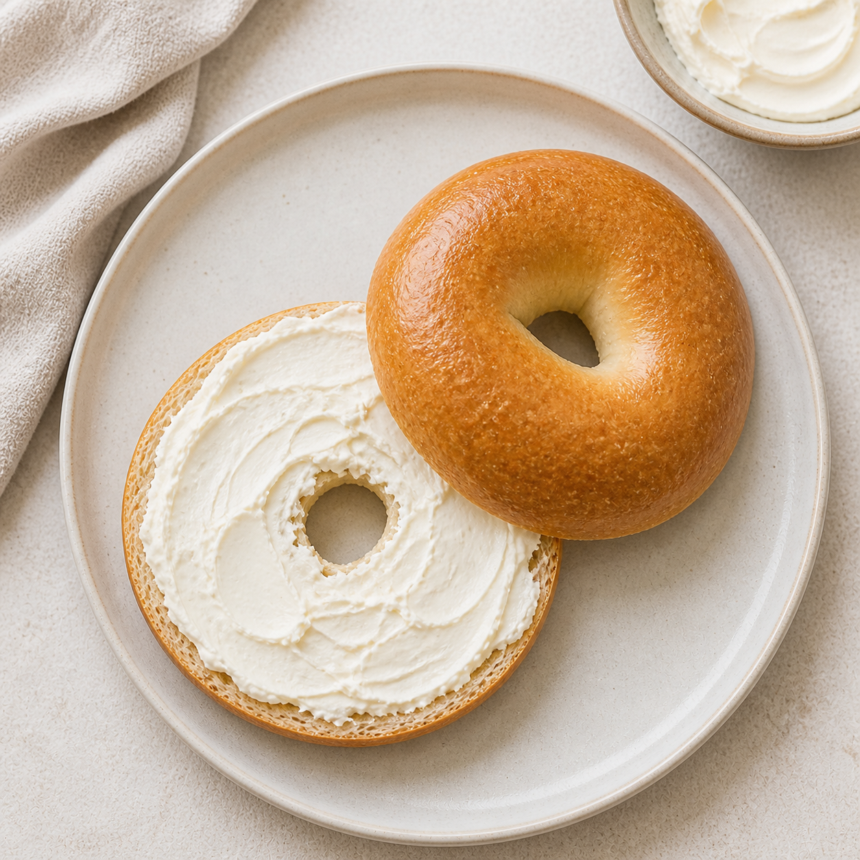 Sliced plain bagel with a layer of cream cheese on a light plate